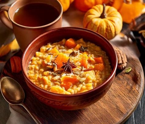 "A warm bowl of oatmeal featuring creamy pumpkin puree, topped with a sprinkle of cinnamon, nutmeg, and chopped walnuts, drizzled with maple syrup, evoking a cozy autumn vibe."