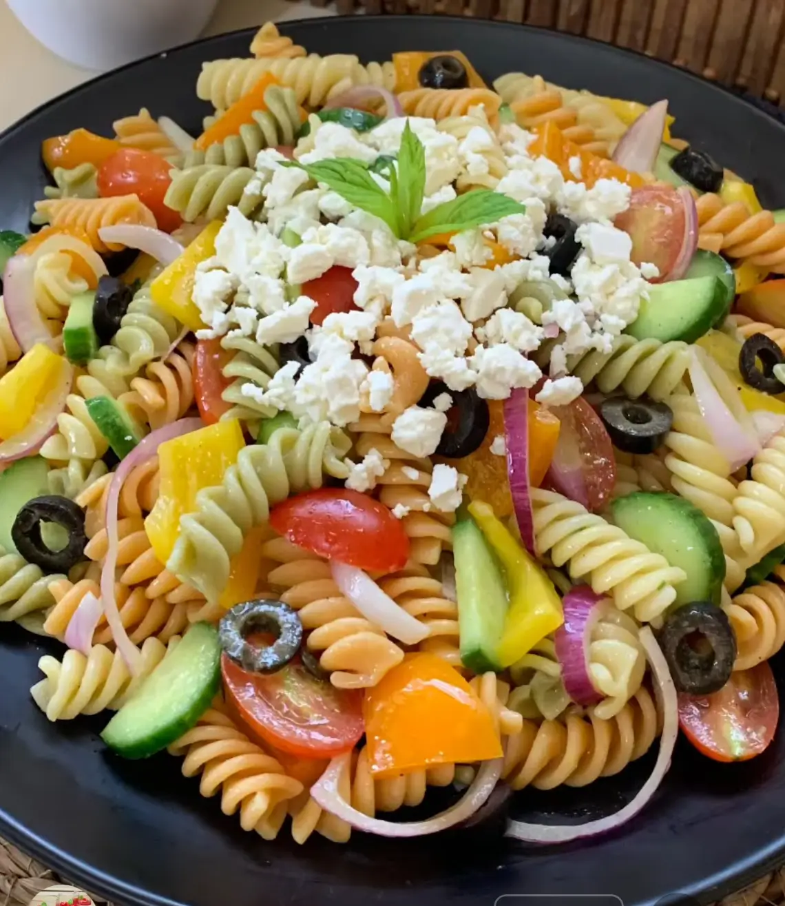 Colorful pasta salad with cherry tomatoes, cucumber, and red onion, drizzled with dressing.